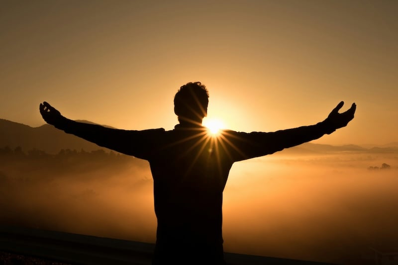 Person with open arms in worship at sunset